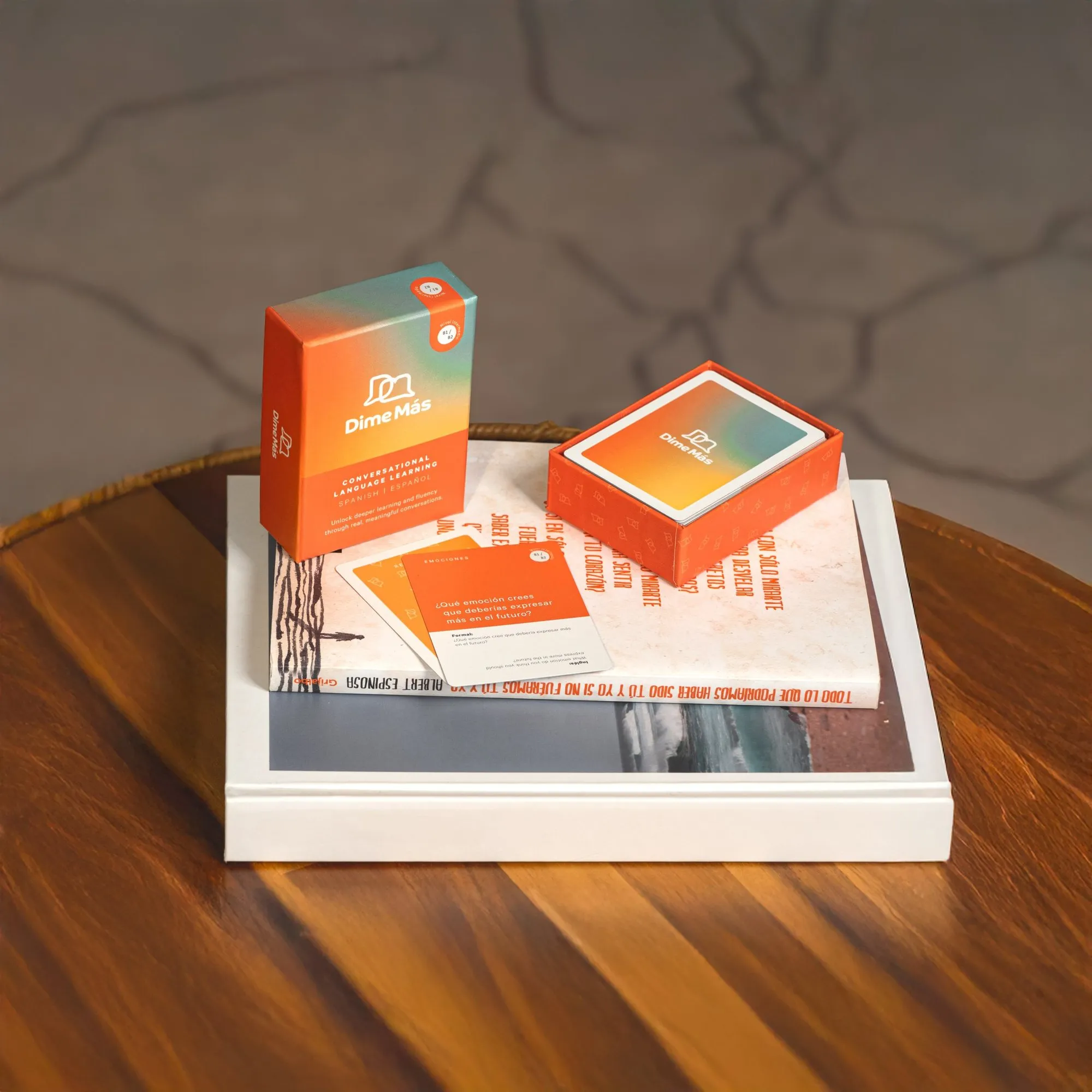 Dime Más card boxes and cards on a pile of books on a wooden table