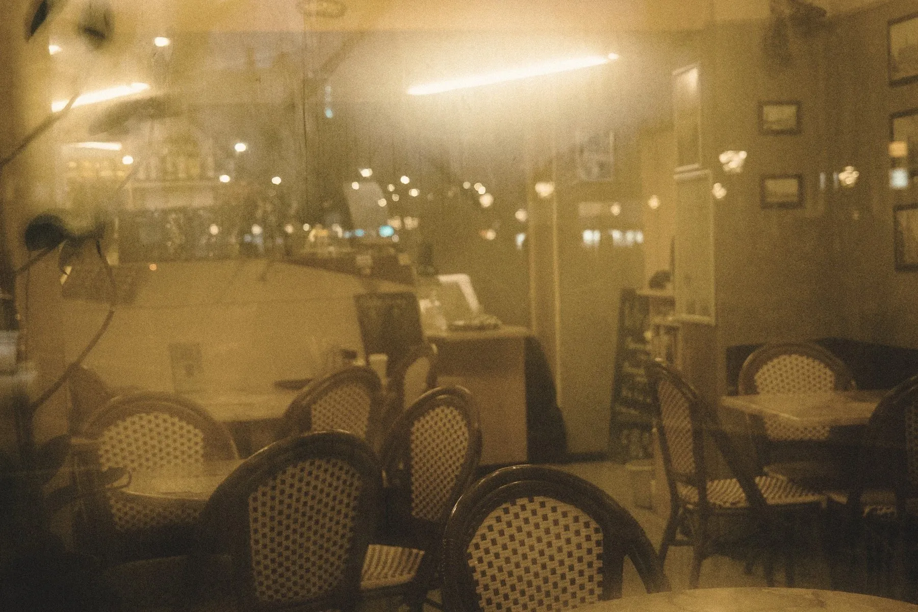 A warm café seen through a window, empty chairs and soft lights inside