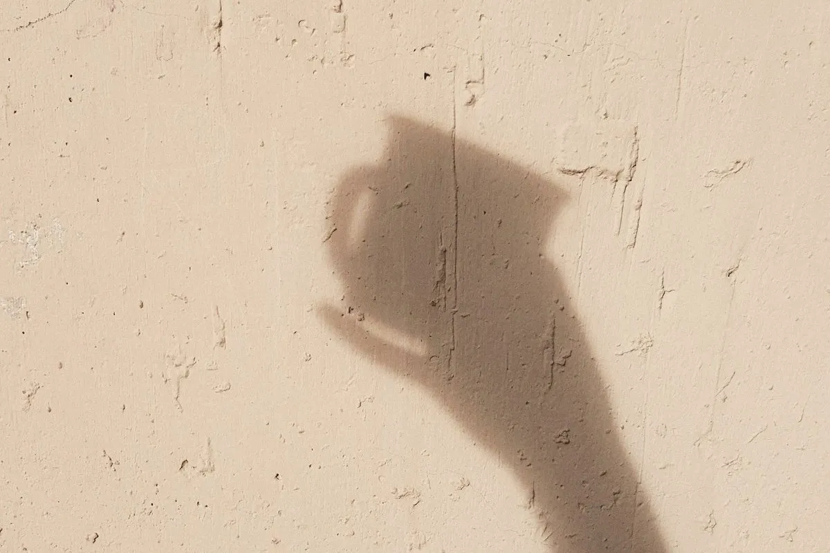 The shadow of a hand holding a cup on a warm plaster wall