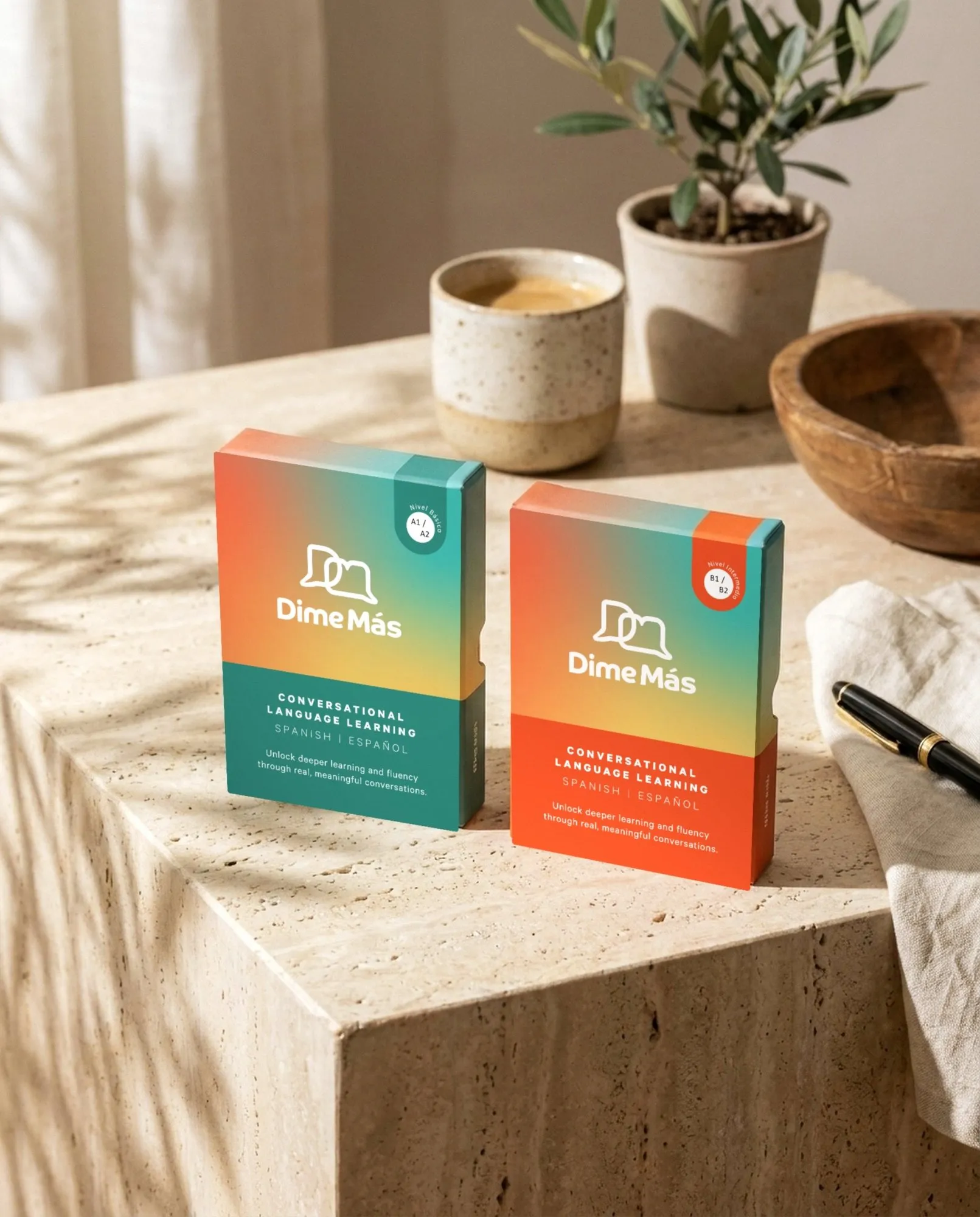 Two Dime Más card boxes on warm stone with soft leaf shadows.