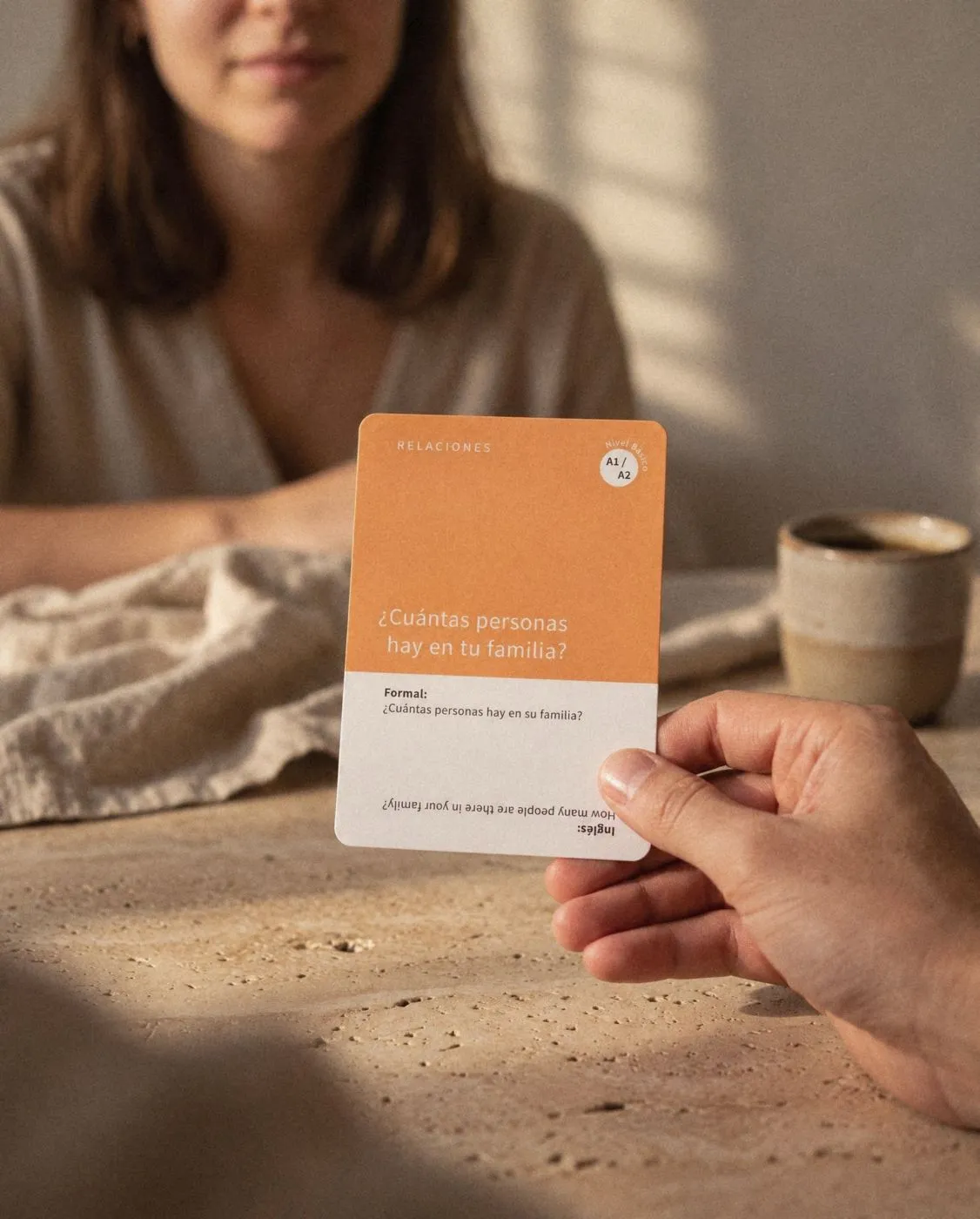 A Dime Más question card held out across a table, ready to ask.