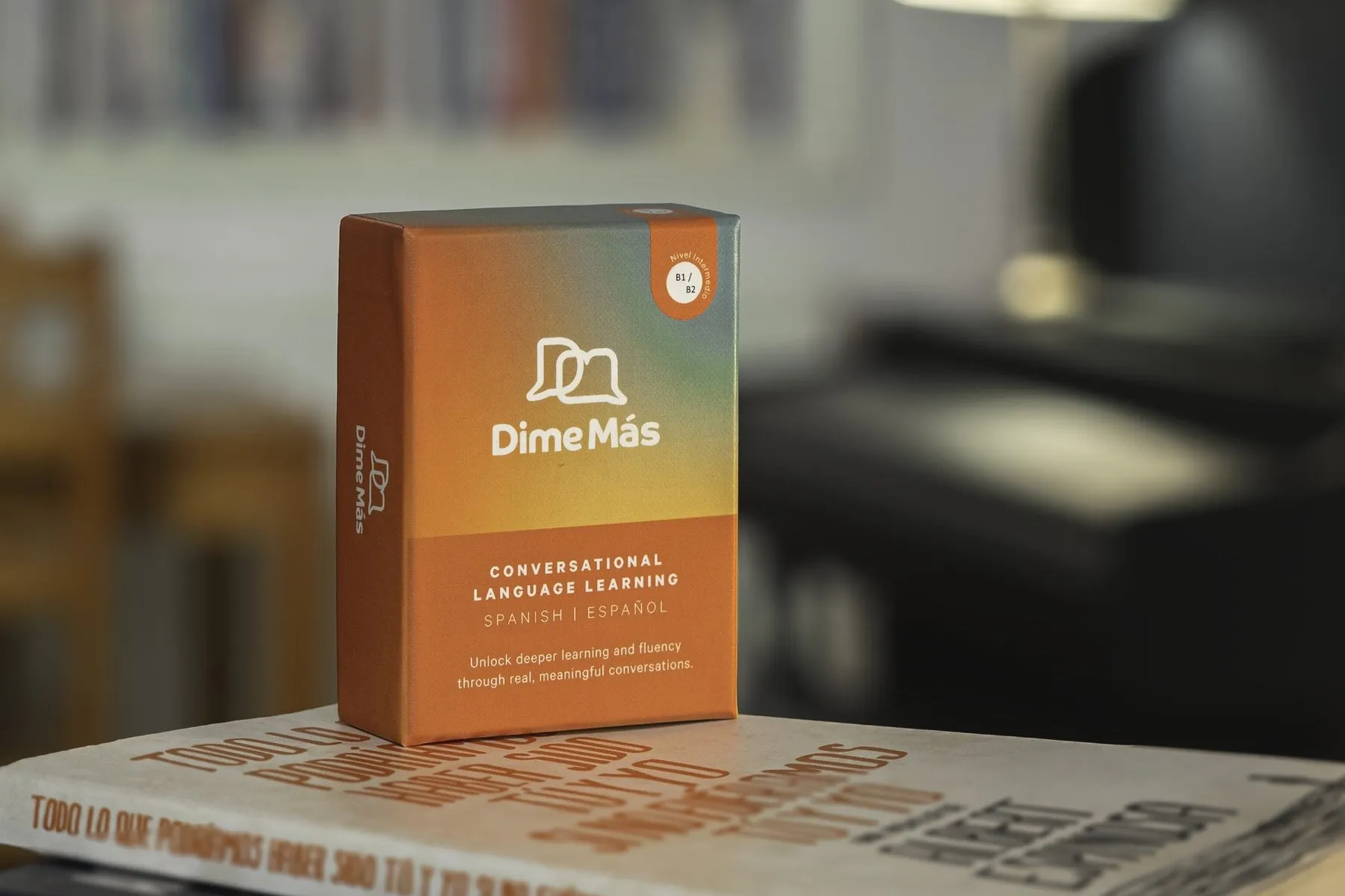 A Dime Más box on a pile of books in a room lit by a warm lamp