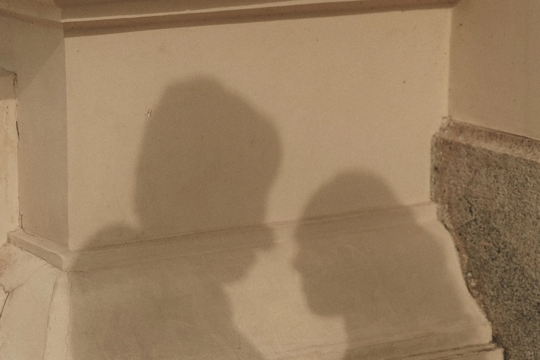 The shadows of two people leaning close on a warm cream wall